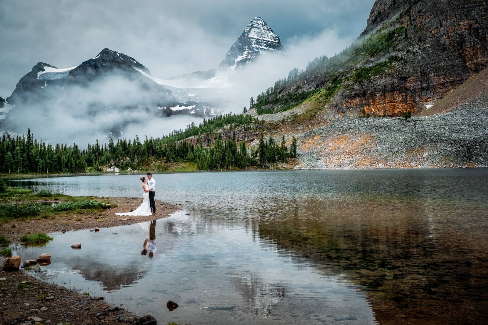 Bride and groom and reflection of Mount Assiniboine in the lake.