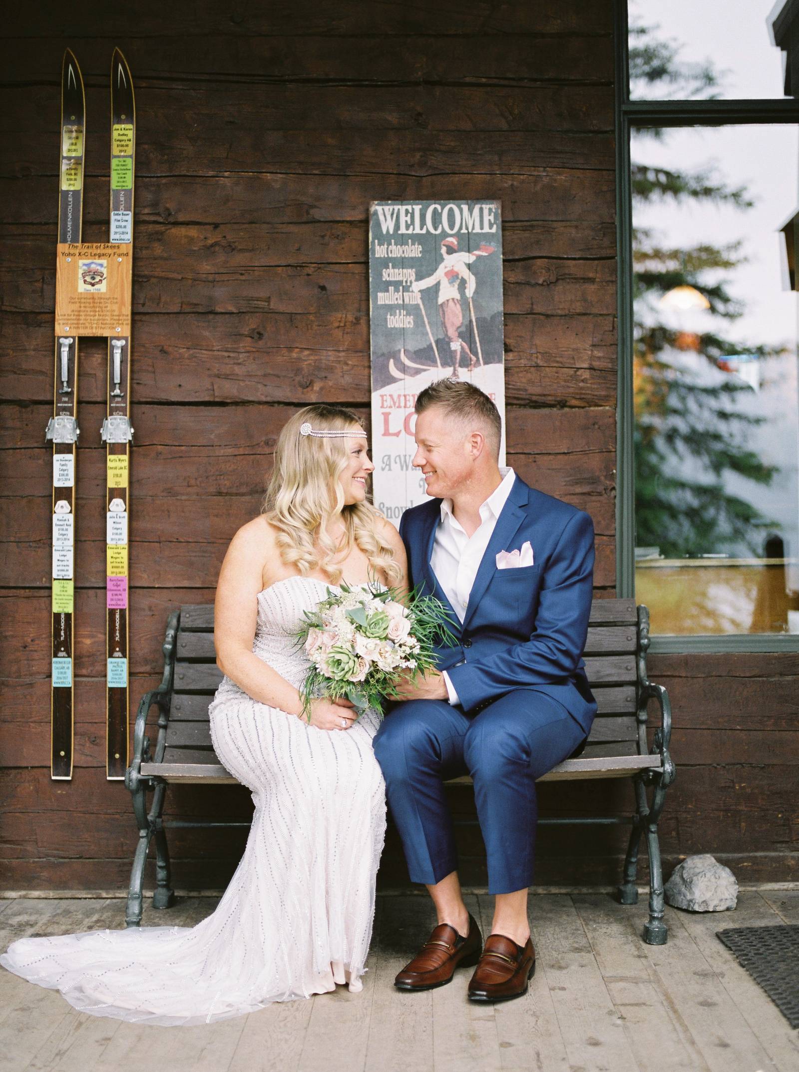 a bride and groom sitting on a wood bench outside the iconic Emerald Lake Lodge