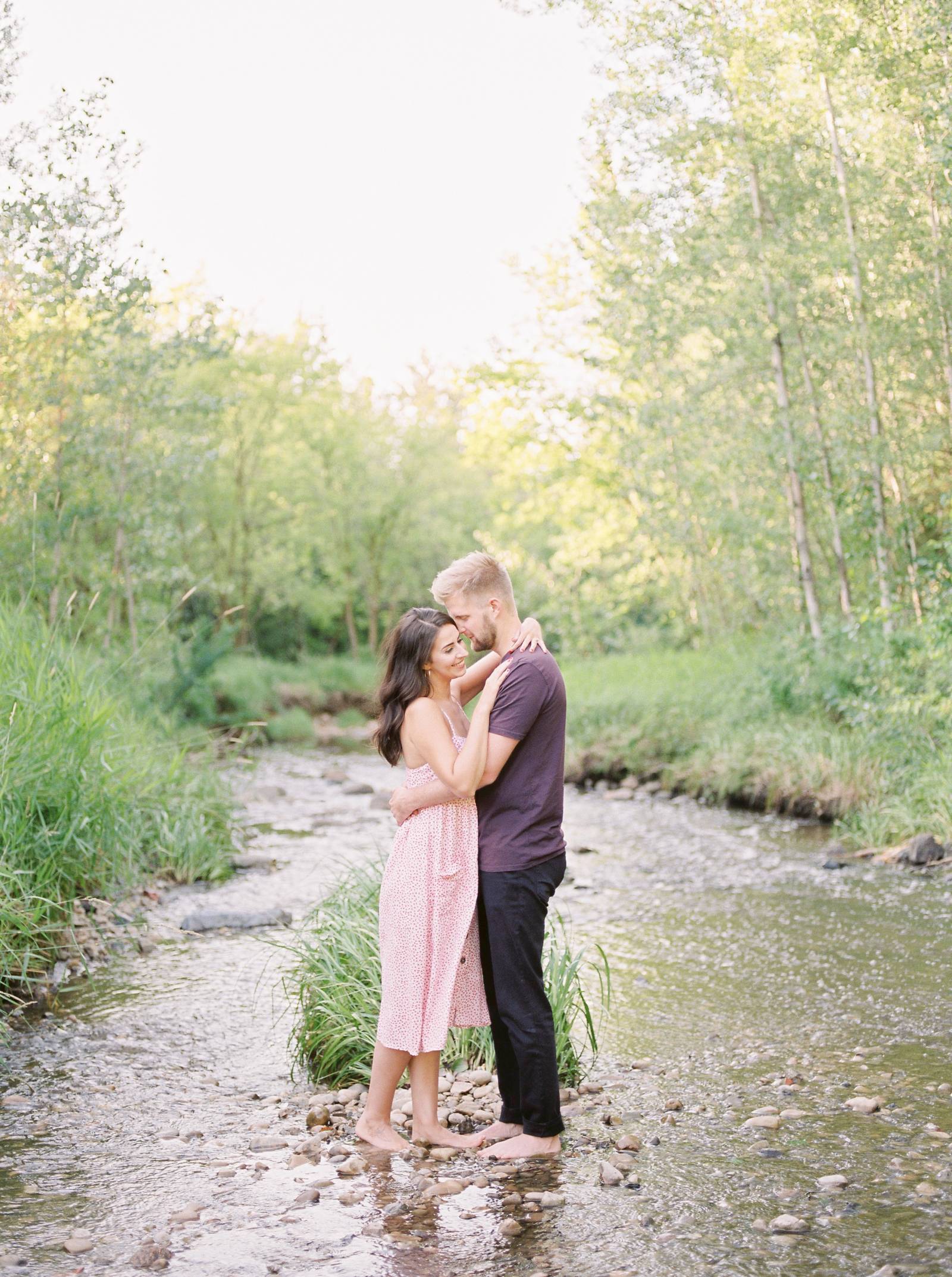 a young man tenderly embraces his fiance on a rocky bank of a spring stream
