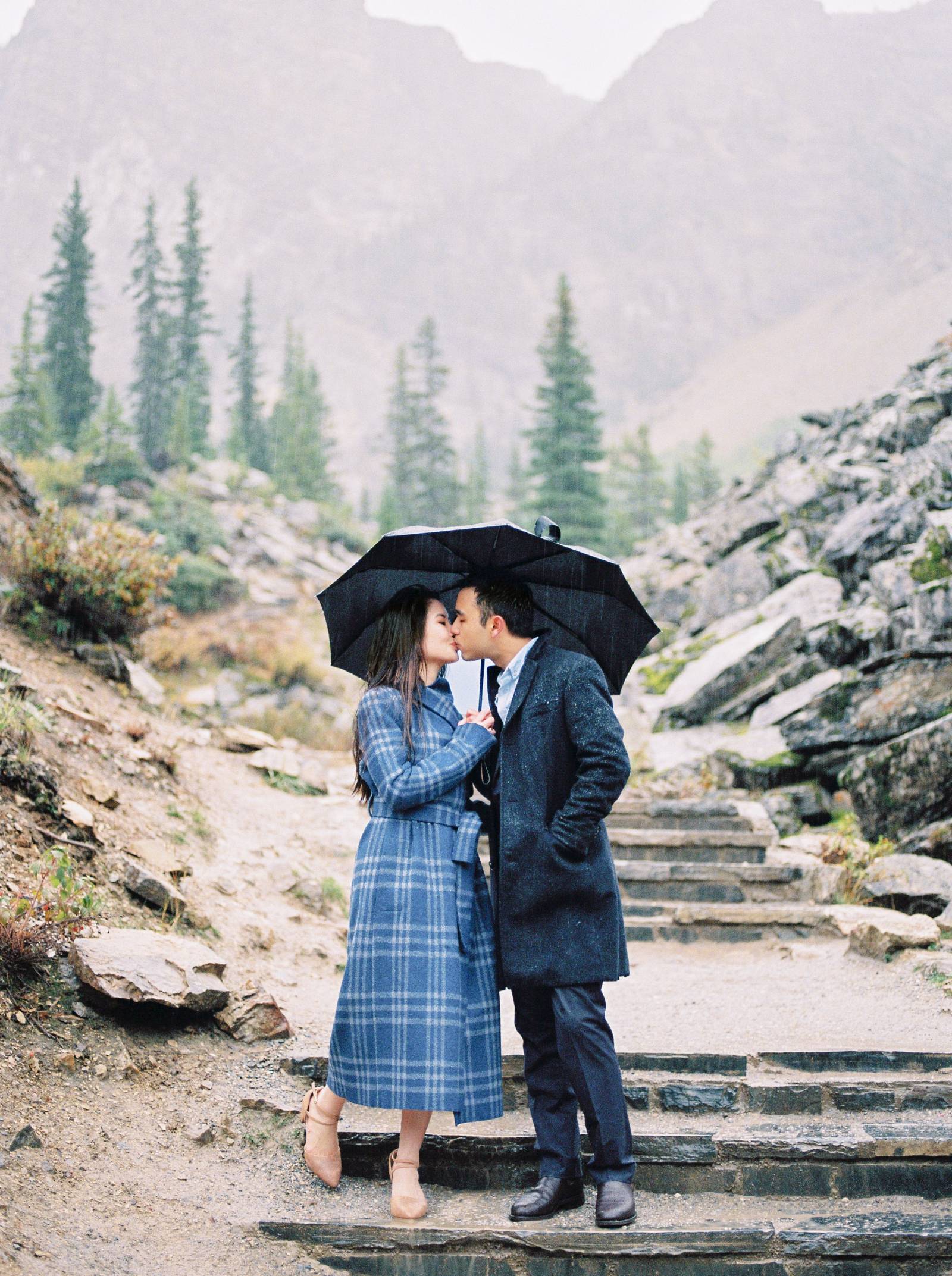 a couple snuggle up under and umbrella during a rain storm at Lake Moraine