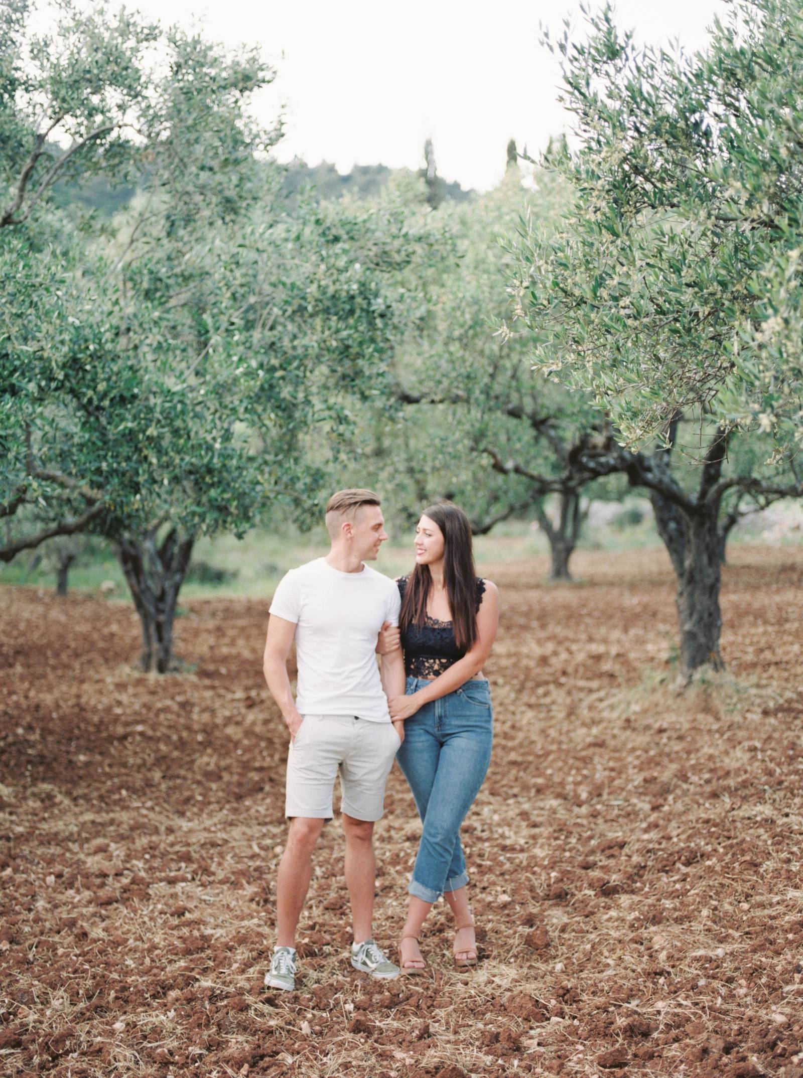 see a young couple walking hand and hand through a olive grove