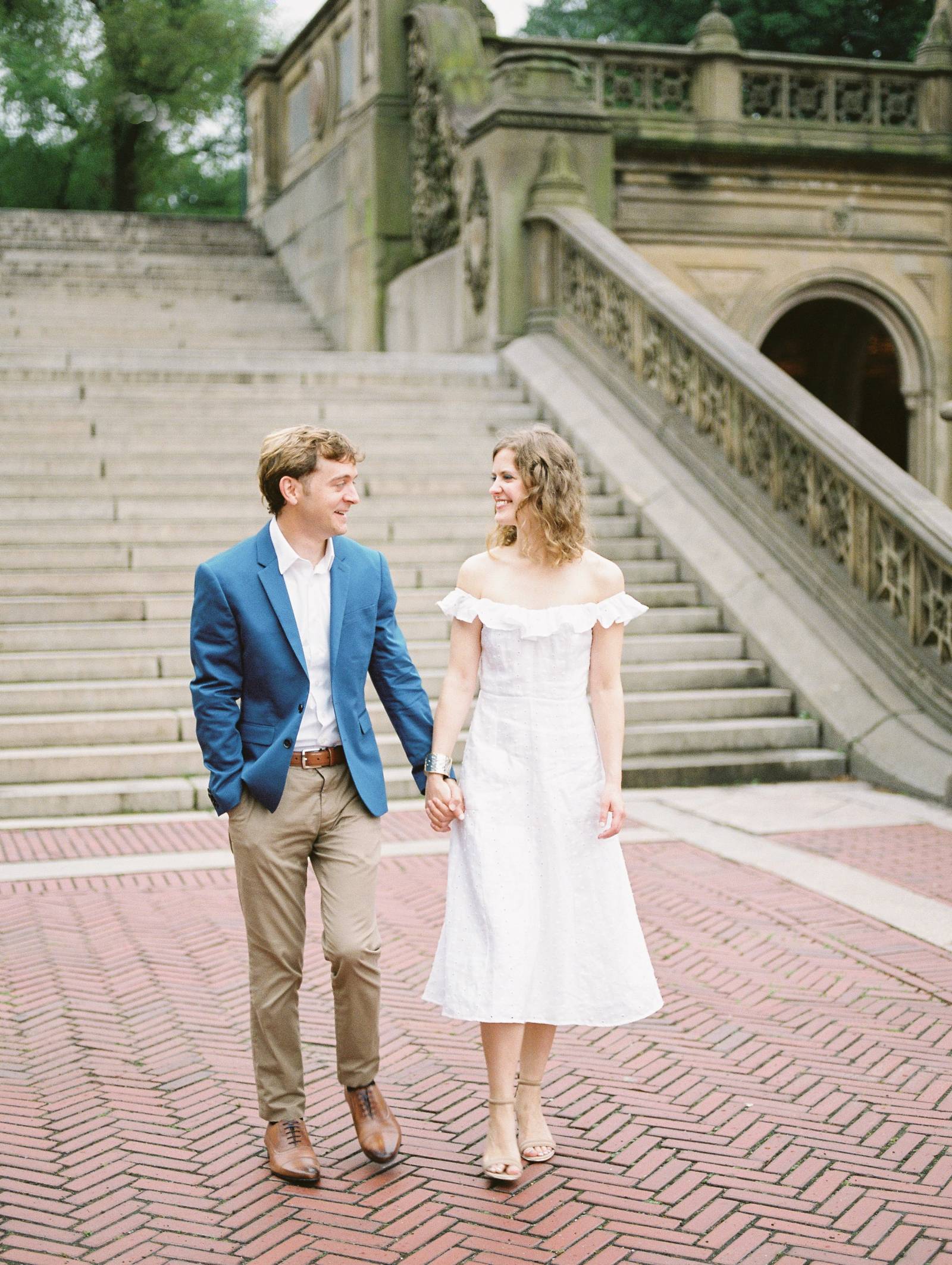 see a young classy engaged couple walking hand and hand through New York Central Park