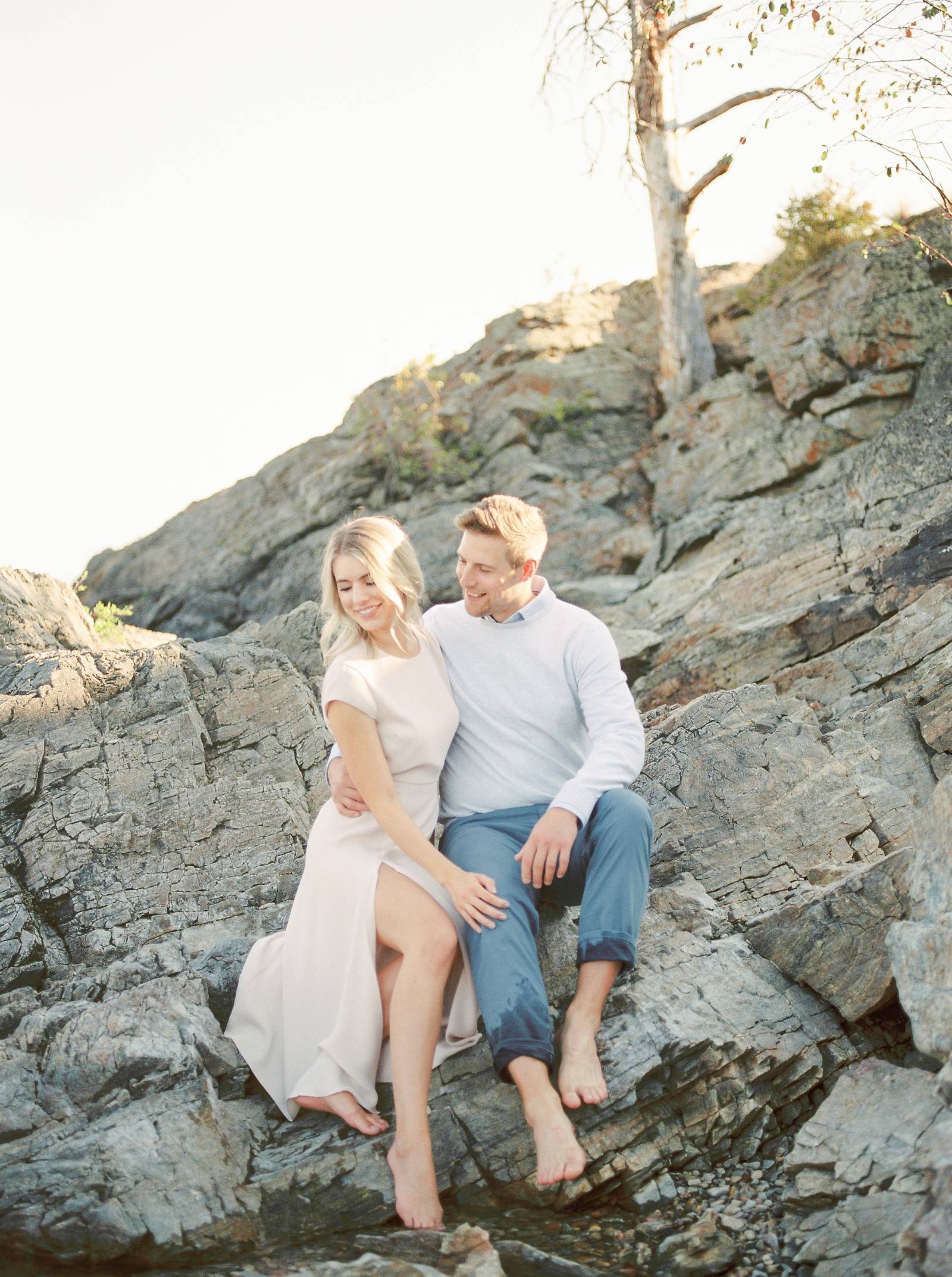a elegant engaged couple sitting on the rocky beach of scenic Kelowna British Columbia