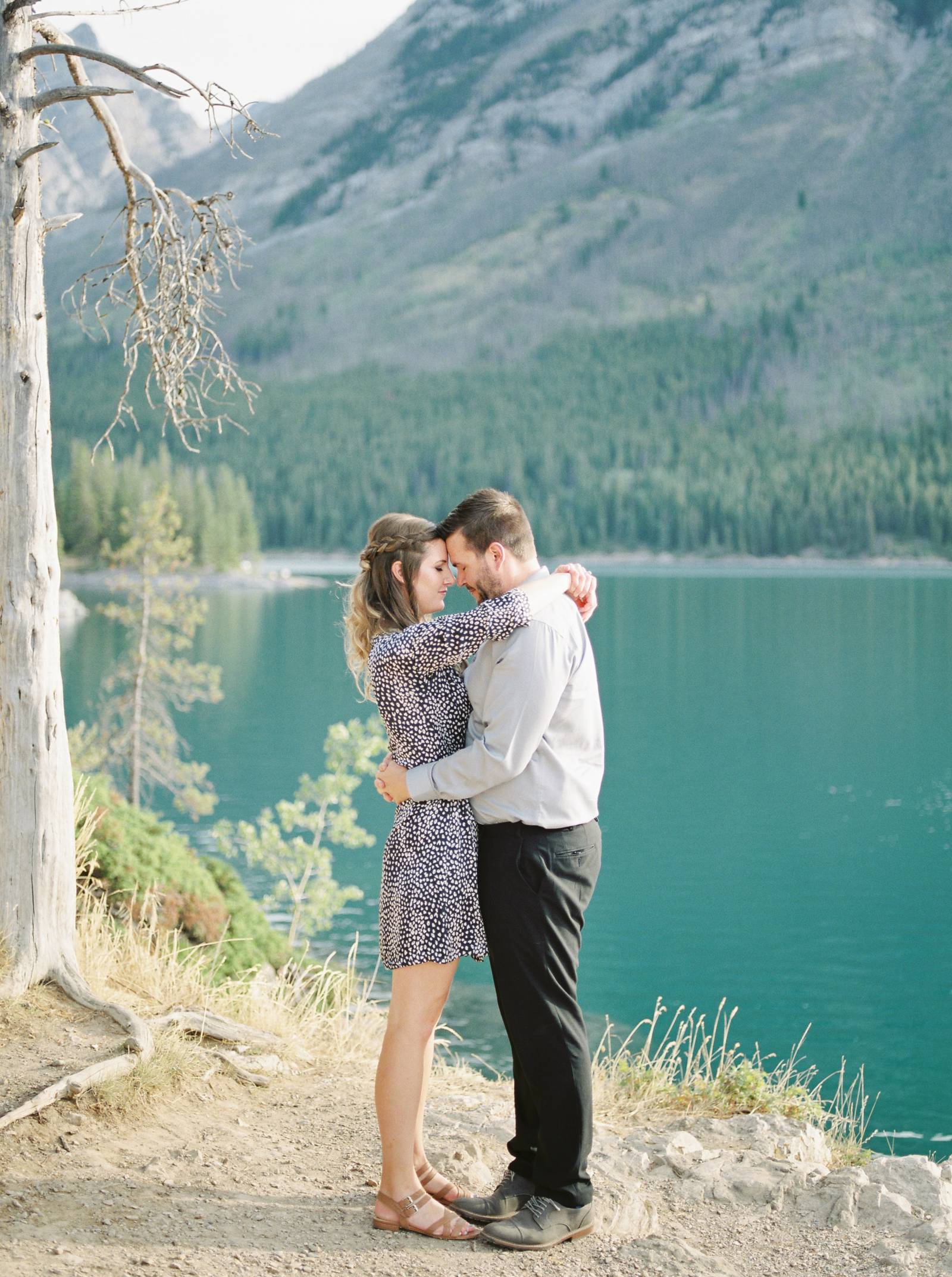 a engaged couple wrap their arms around each other lovingly as the sun rises over Lake Minnewanka
