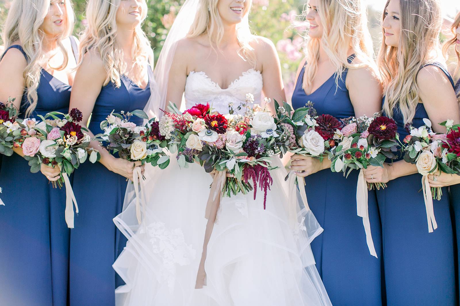 Carly is Standing with Her Bridemaids and Holding April Flowers | The Wedding Standard