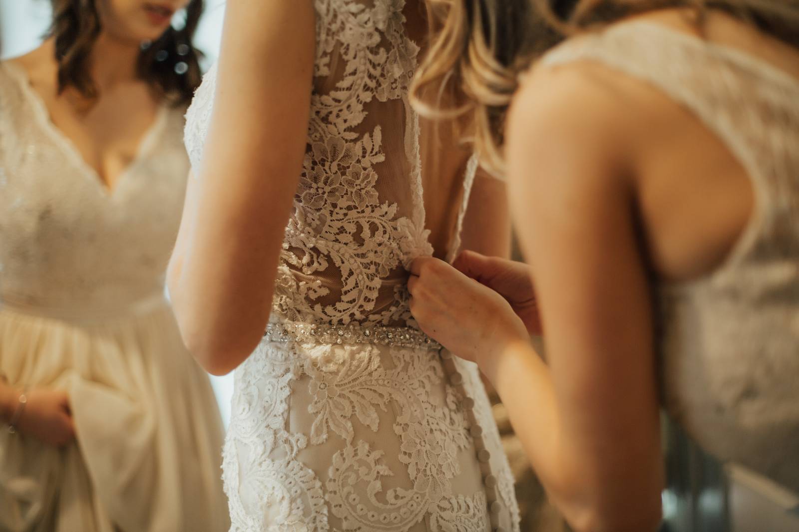 bridesmaid buttoning up laced wedding gown for bride