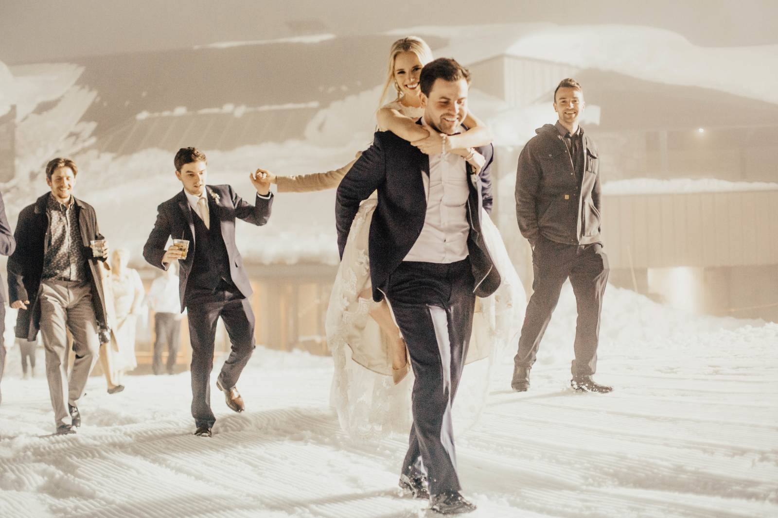 groom giving bride a piggyback through the snow