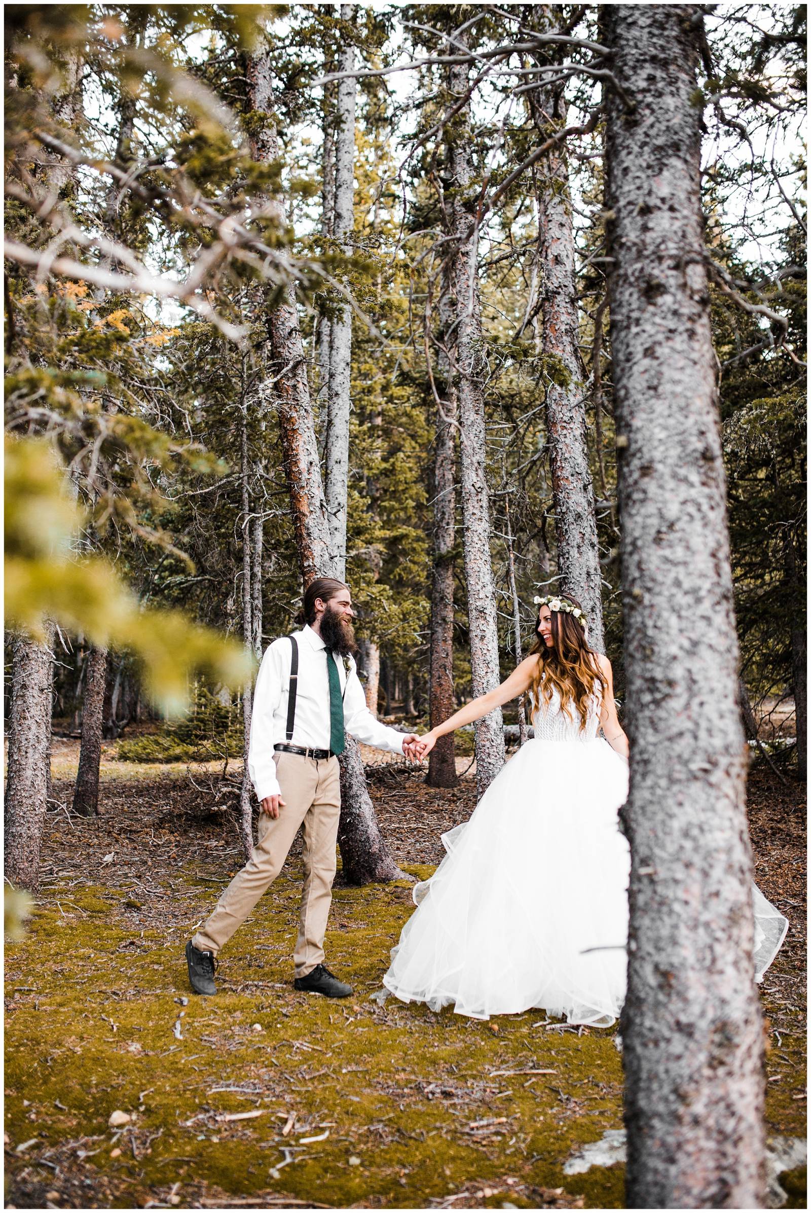 bride leading groom through Colorado forest | groom in green tie and suspenders