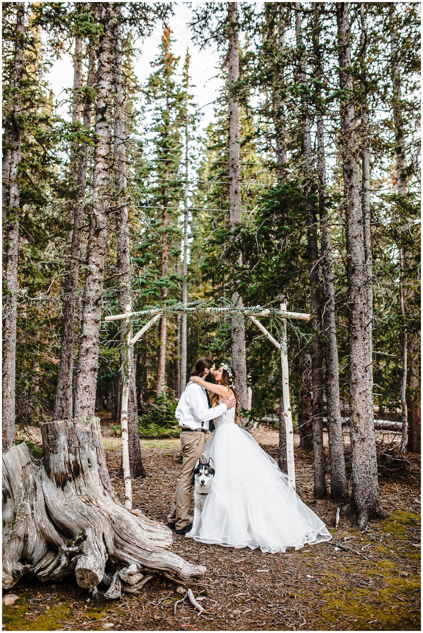 bride and groom kissing under mountain ceremony arbor with their dog