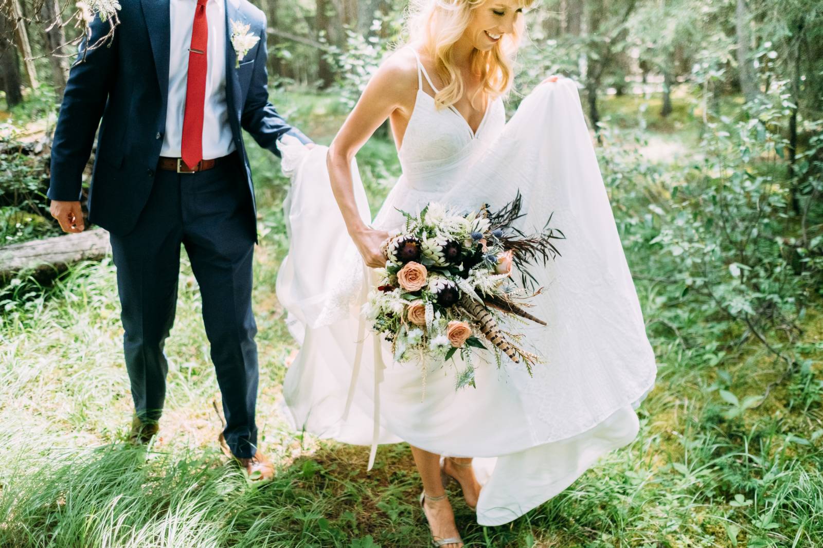 groom holding up the train on bride's Hayley Paige wedding gown while she walks and holds wedding bo