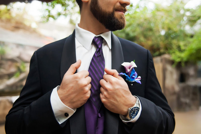 groom in purple tie holding jacket