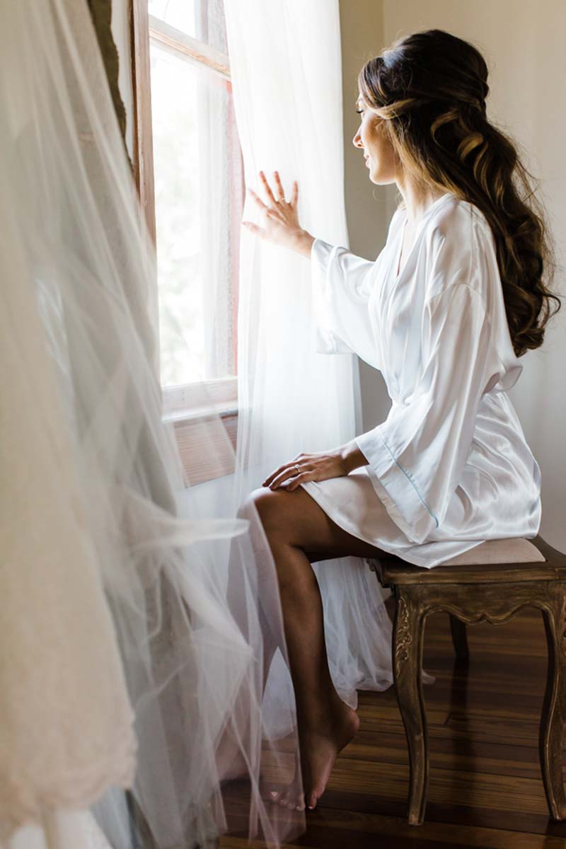 bride holding back curtains looking out window