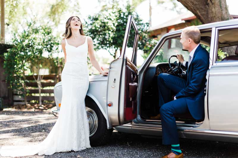 bride laughing in front of old car