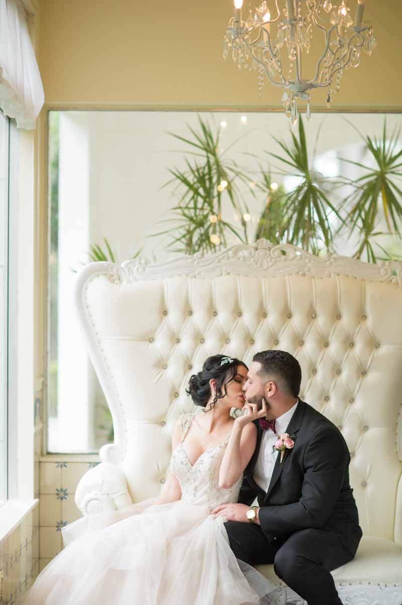 bride kissing groom on high back white loveseat