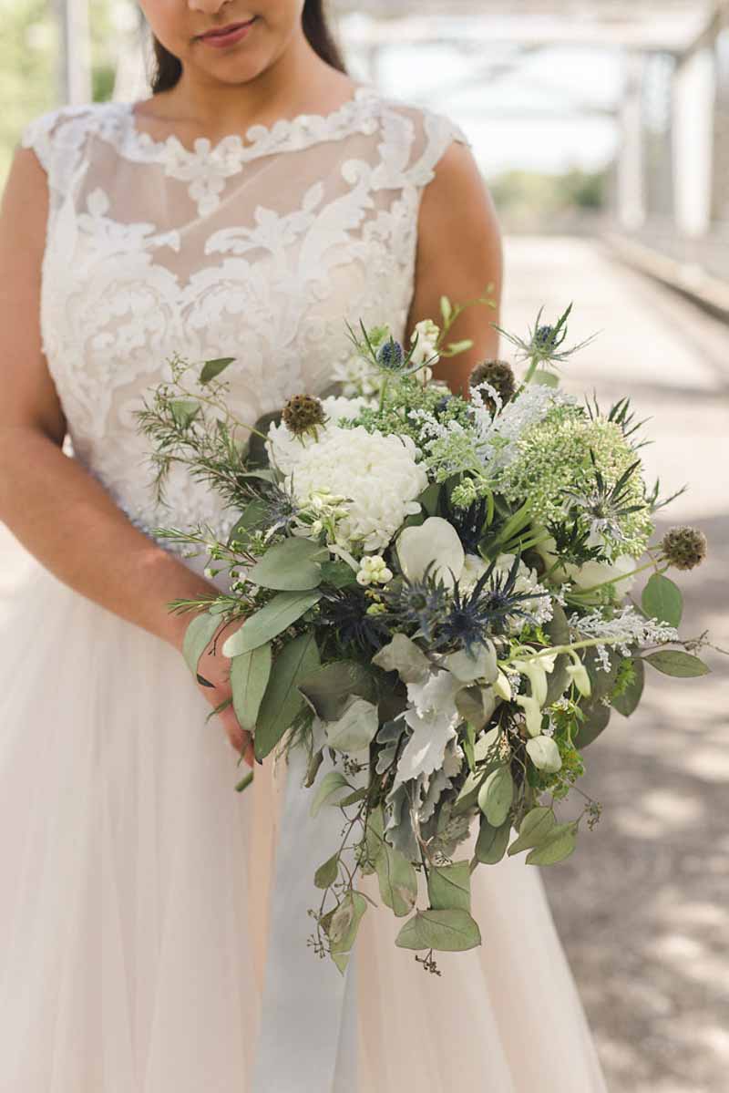 bride holding bouquet with greenery and thistles