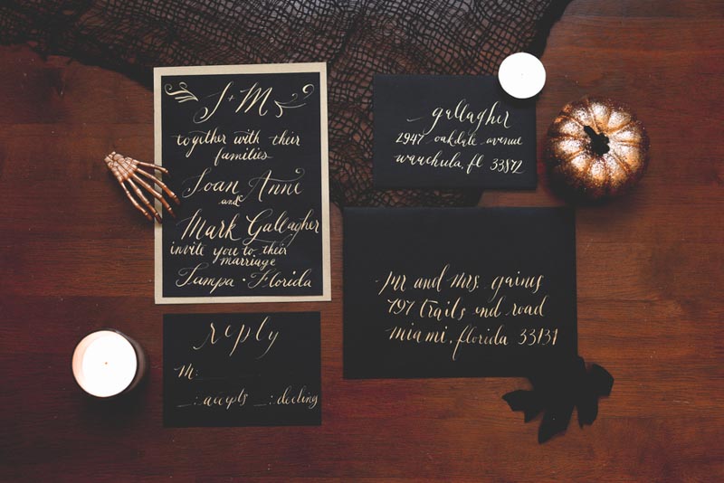 black and gold calligraphy wedding invitations on wood table