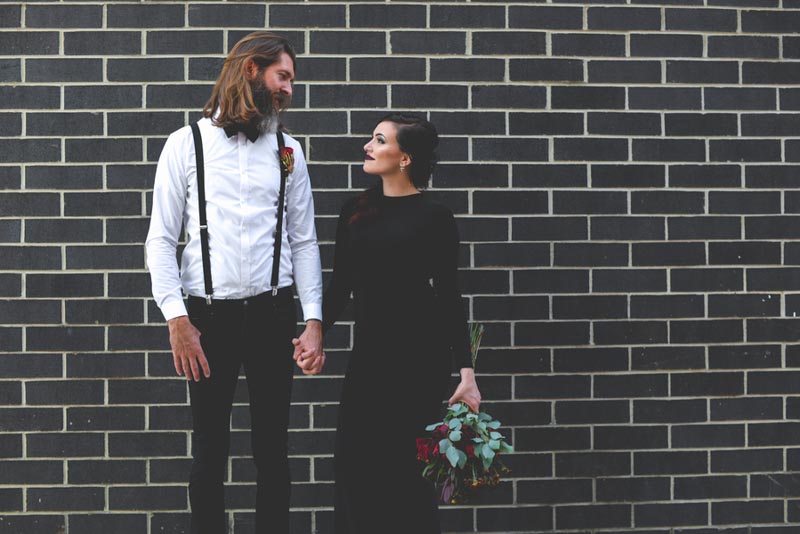 couple holding hand in front of black brick wall