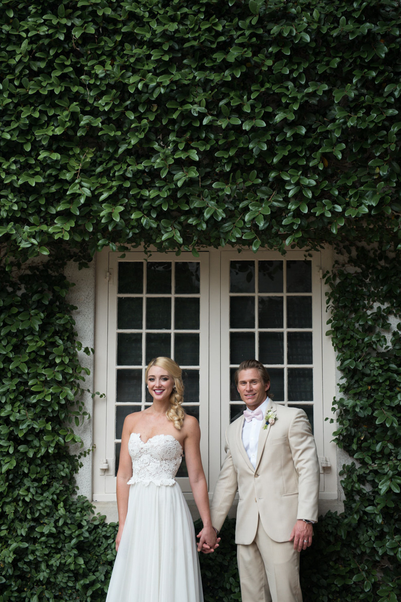 couple holding hands in front of vine covered wall