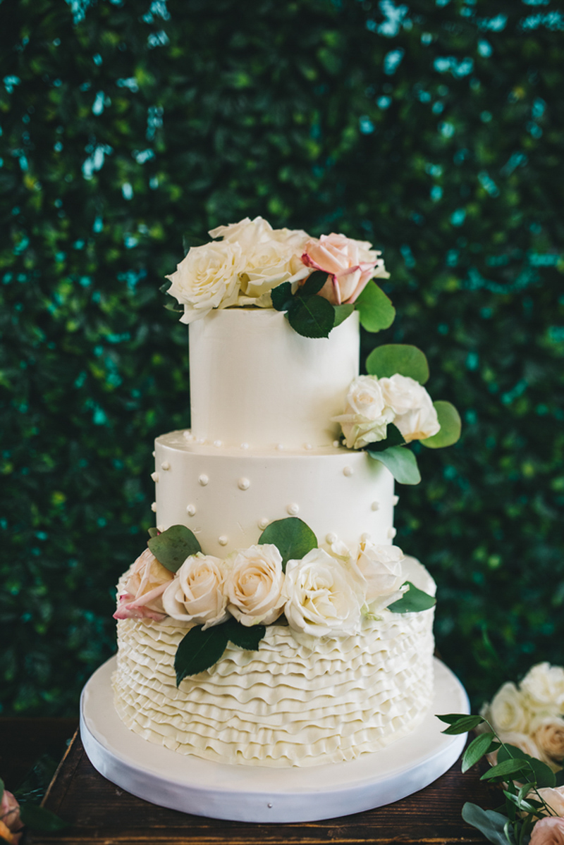 white buttercream wedding cake in front of hedgewall