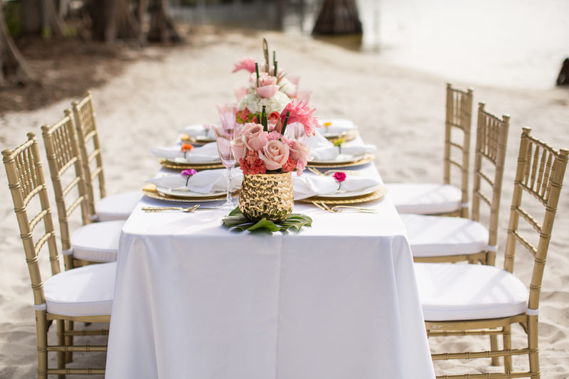 tropical table display with gold chaivari chairs on beach