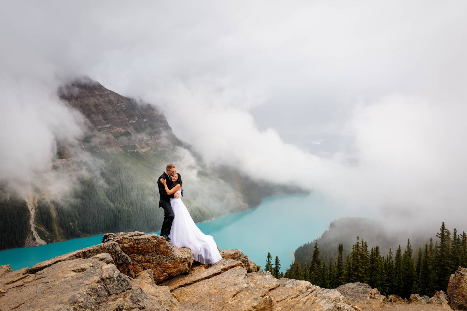 married couple holding each other in the cloudy day at the top of the mountain
