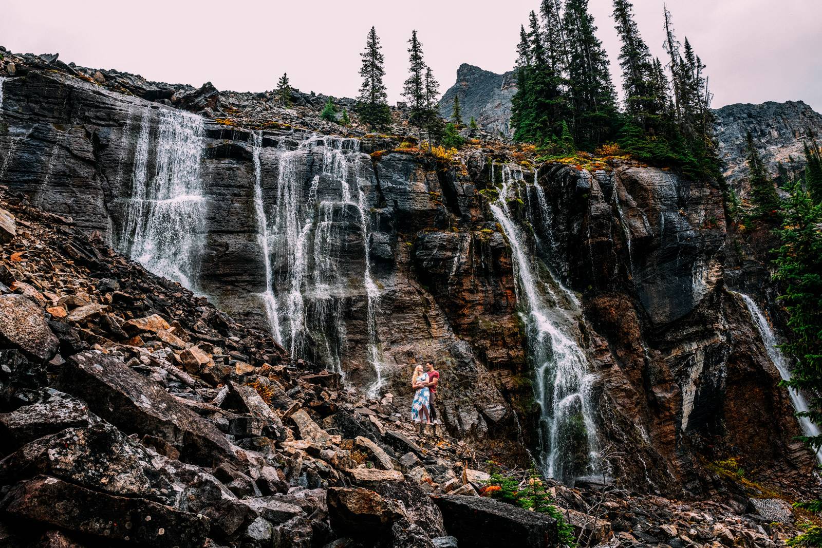 engaged couple standing by the waterfall