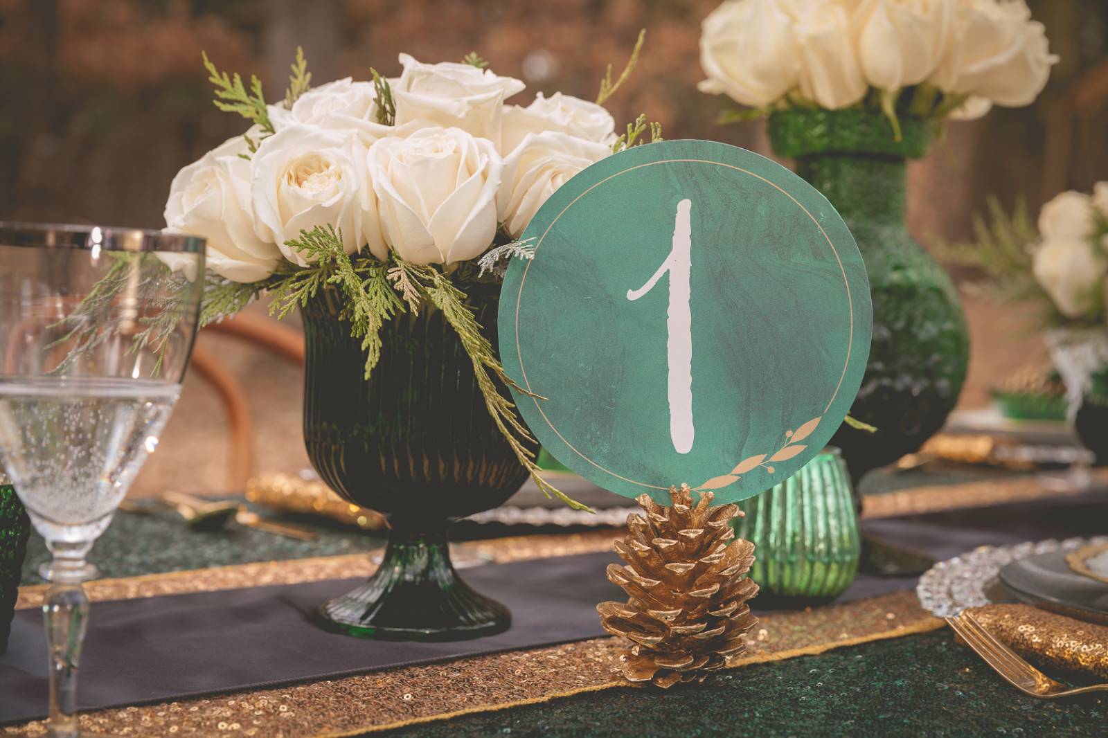 white centerpieces, emerald green table numbers, pine cone decor