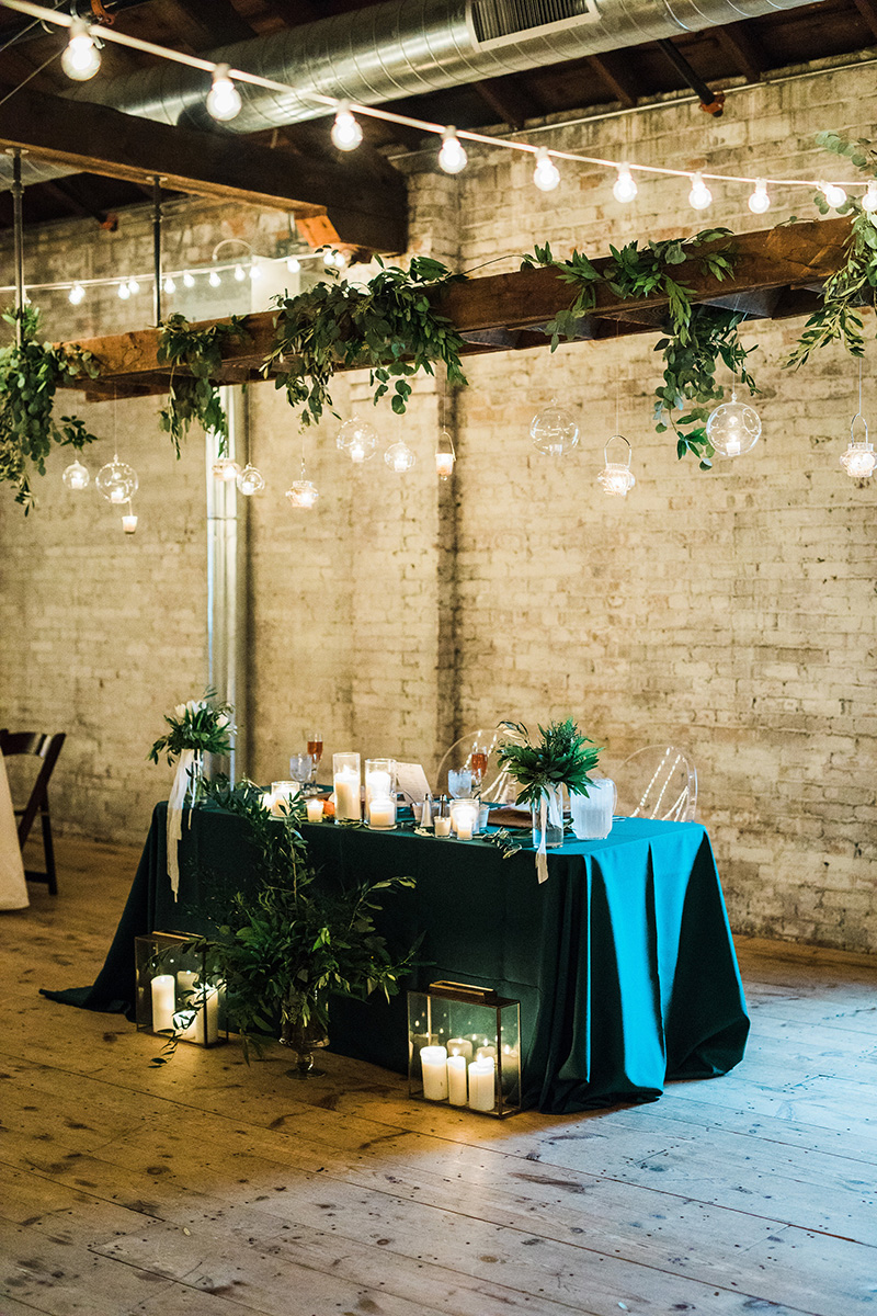 industrial warehouse wedding, sweetheart table, ghost chairs, cafe lighting wedding greenery