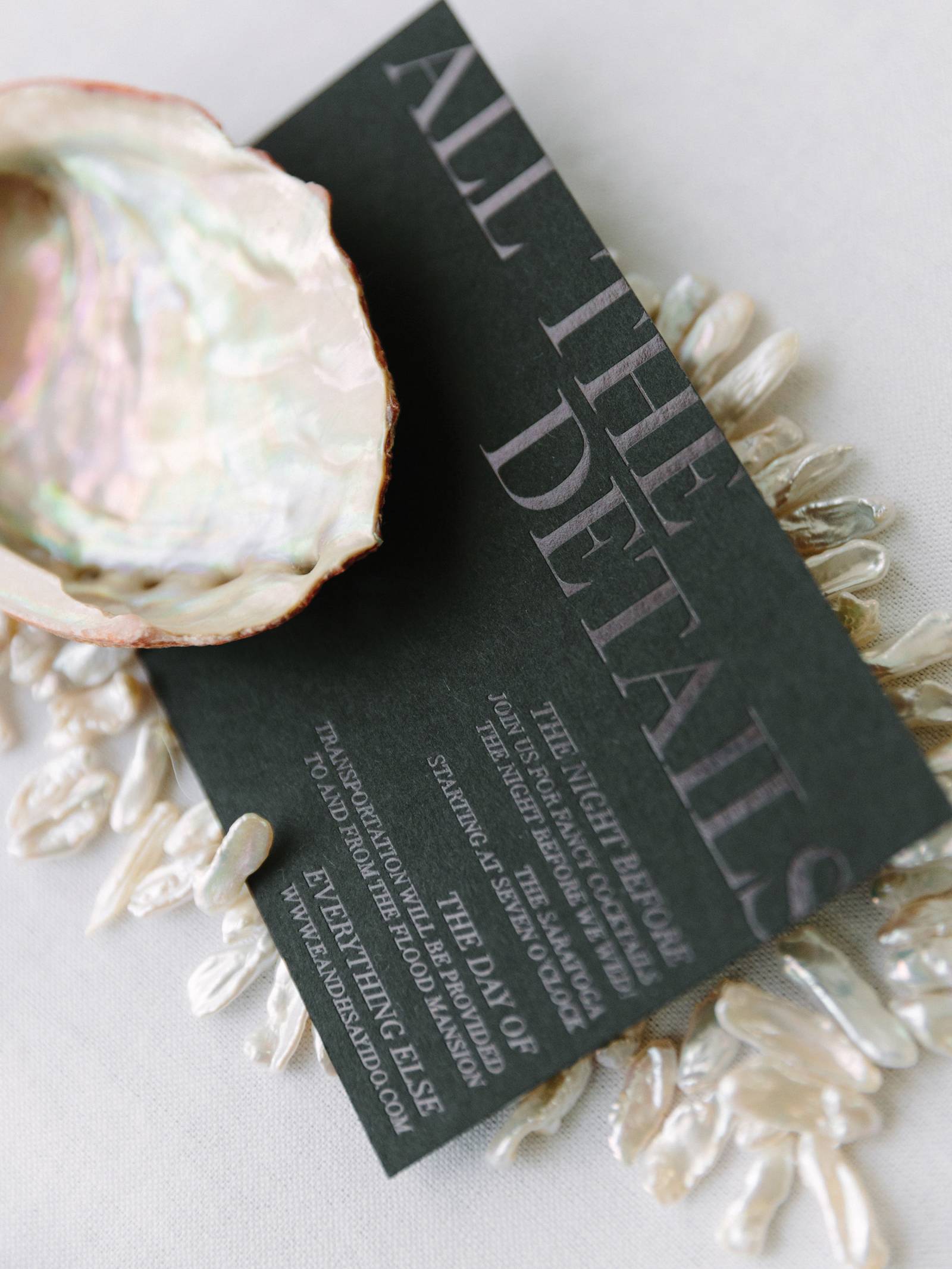 Black wedding stationery enclosure with silver lettering, framed by fresh water pearls and shell.