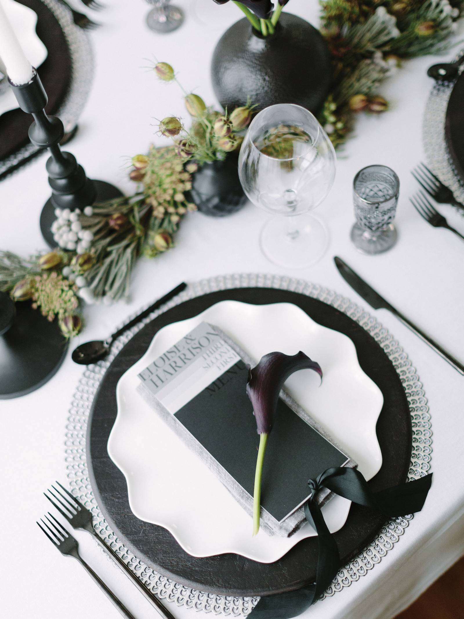 table setting with black and silver chargers, white scalloped plate, black and silver place card and