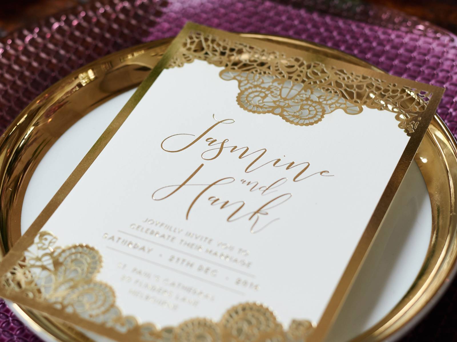 Ornate gold and white wedding invitation on gold rimmed plate and violet charger