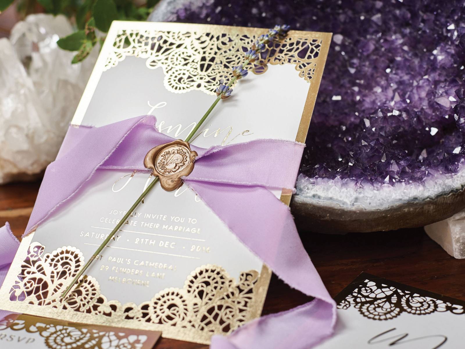 Elegant gold and white wedding invitation wrapped with lavender ribbon and stem of fresh lavender