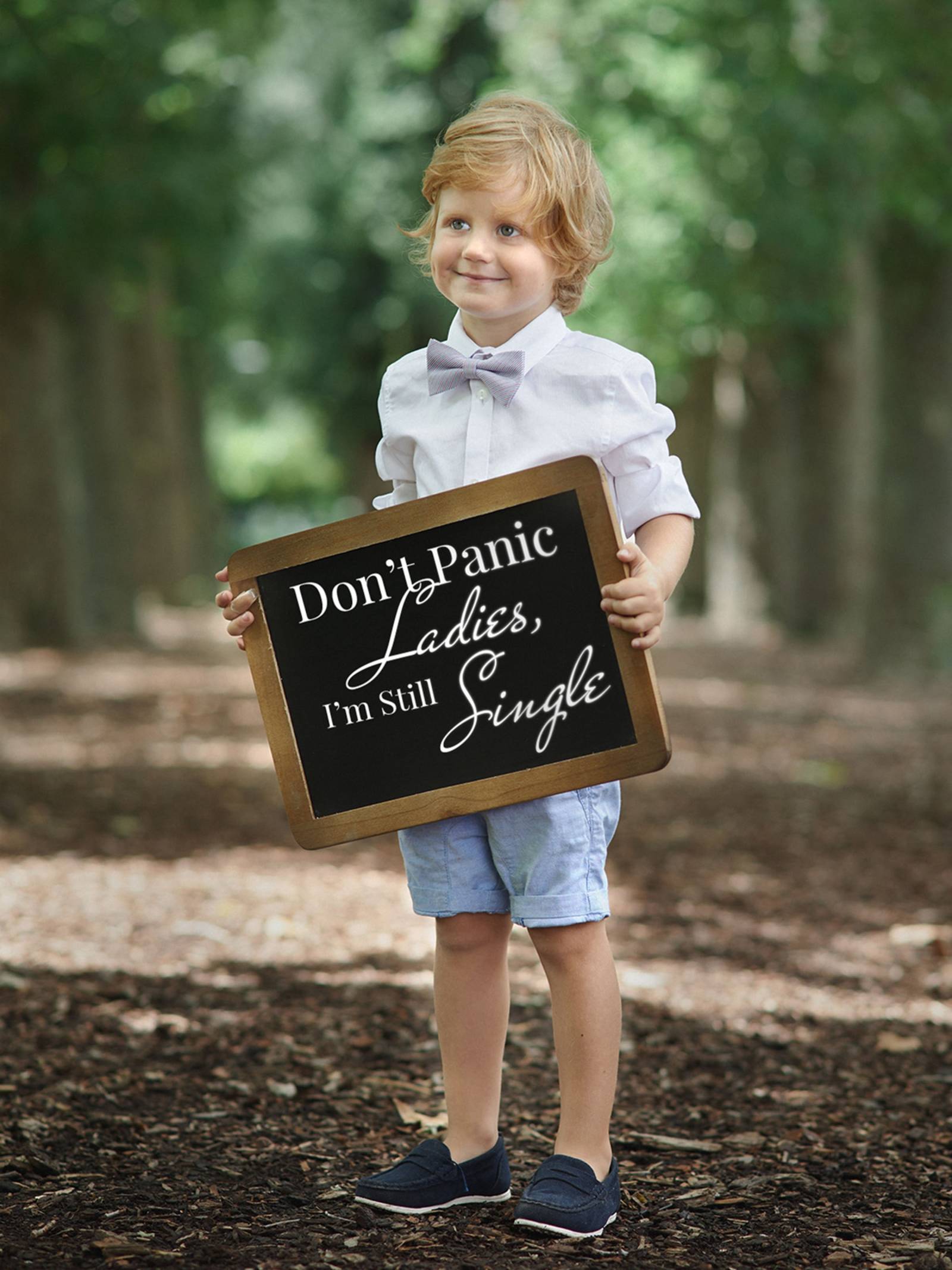 Ring bearer in white shirt, bow tie and blue shorts holding a sign.