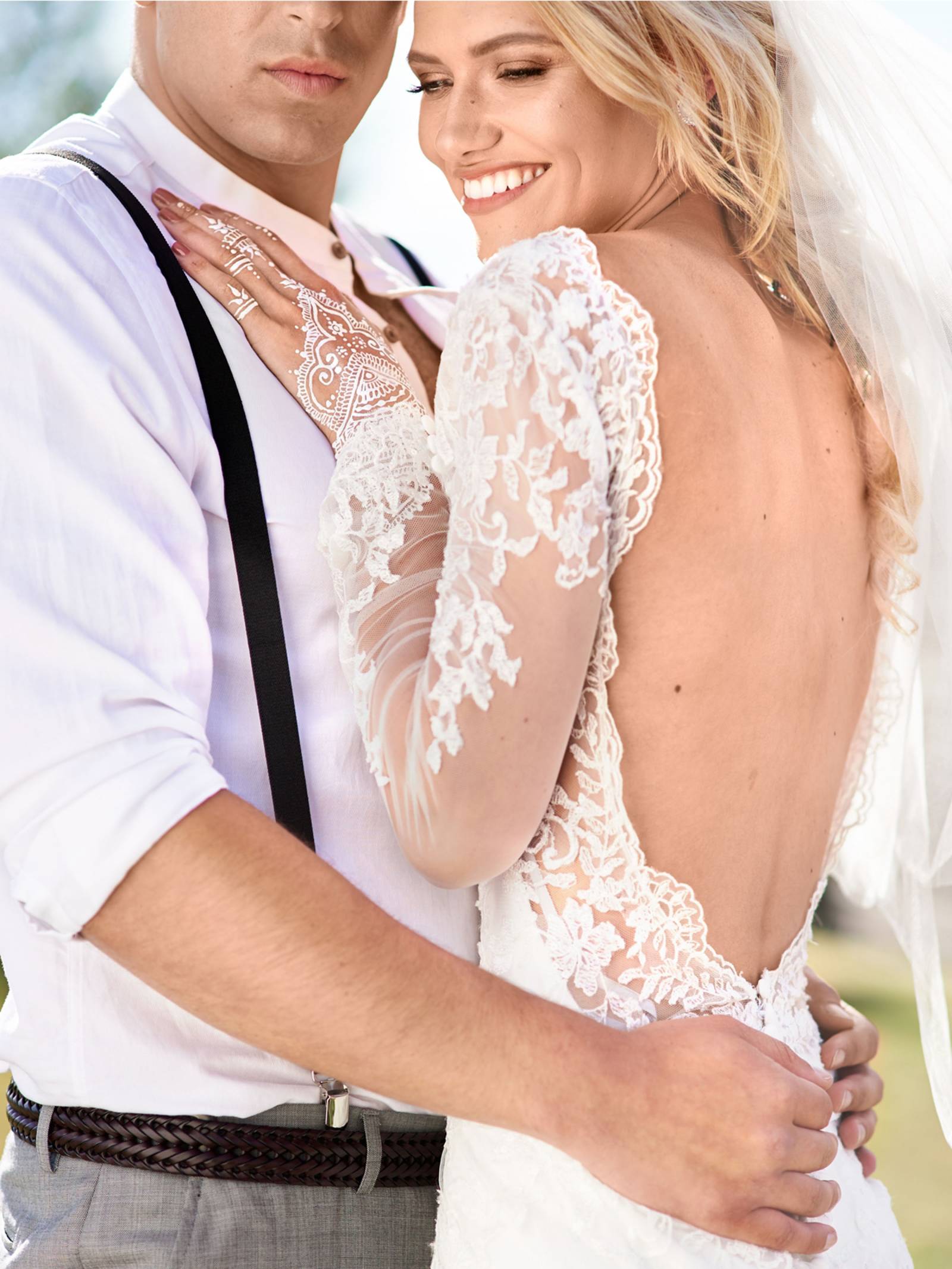 bride in backless wedding gown leaning against groom in lavender shirt with suspenders