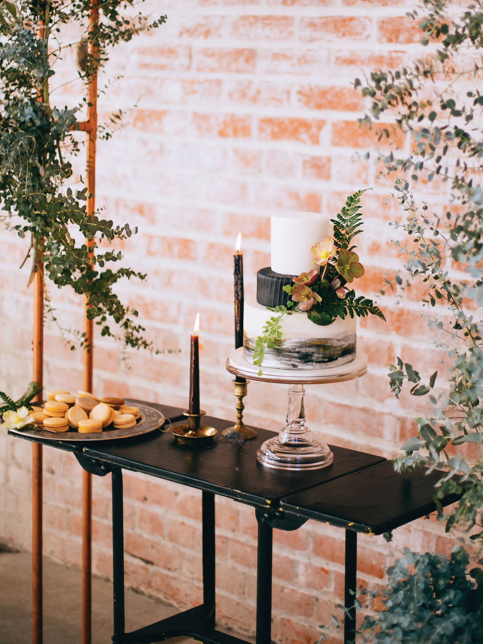 Dessert table with macarons, black and white wedding cake, tapered candles on a black side table