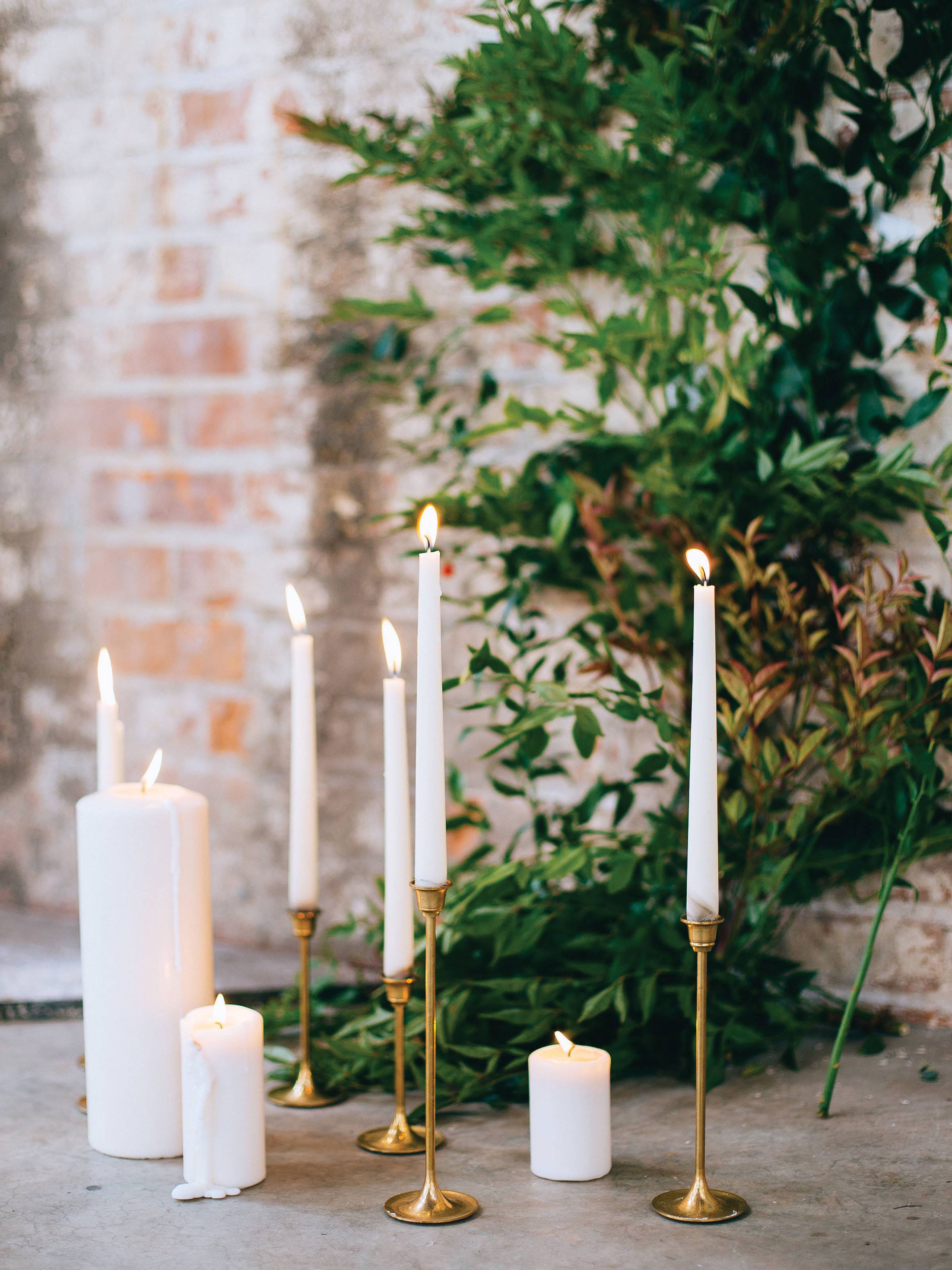 Altar decor of white pillar and tapered candles in gold holders with arch of greenery