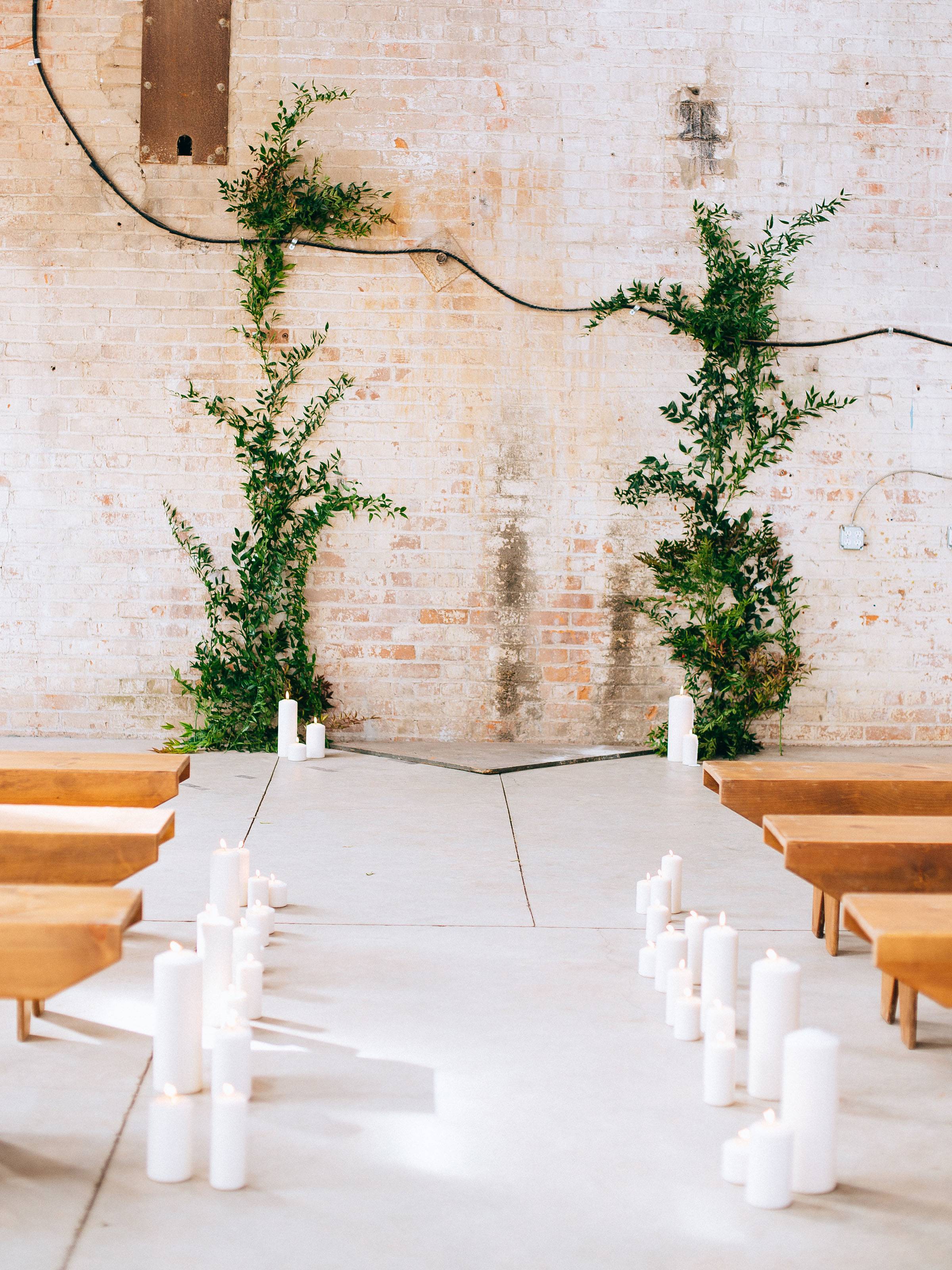 Ceremony aisle flanked with white pillar candles and wood benches and two columns of greenery