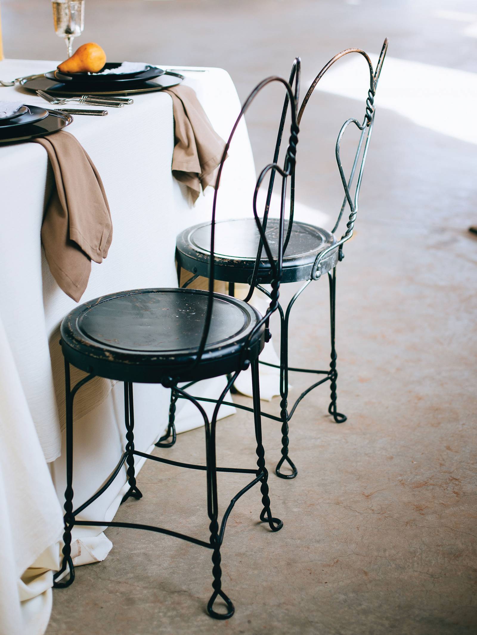 Black bistro chairs by a table draped in white linen with beige napkins and black plates
