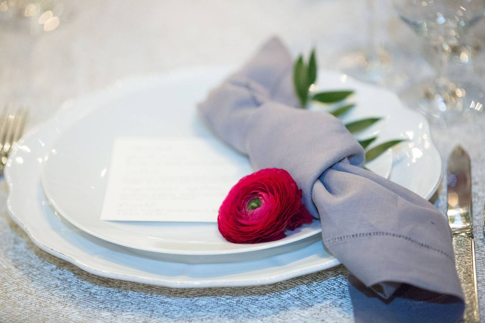 Place setting of white plates, gray napkin and red flower