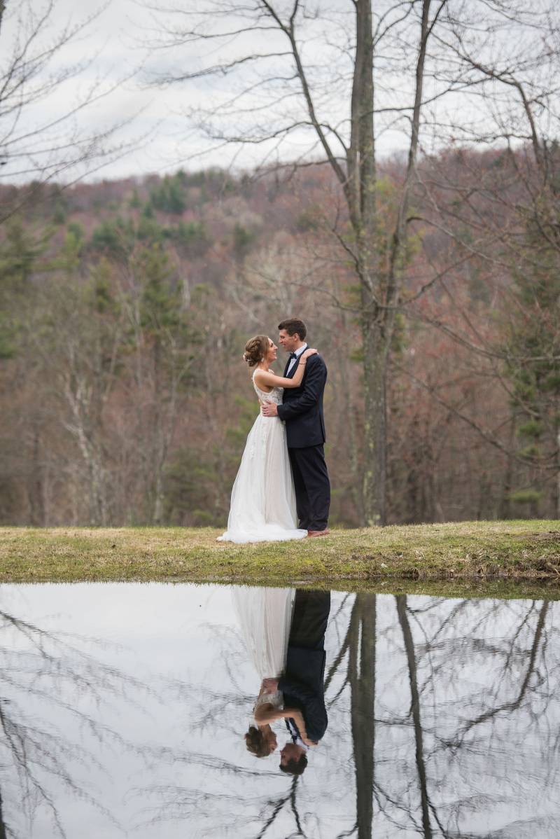 Portrait of bride and groom reflected in pond at Sleepy Hollow Inn in Vermont on spring wedding day