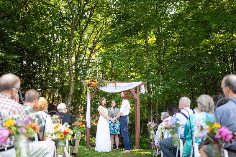 couple saying vows under wedding arch at Trailside Inn with flowers and swag