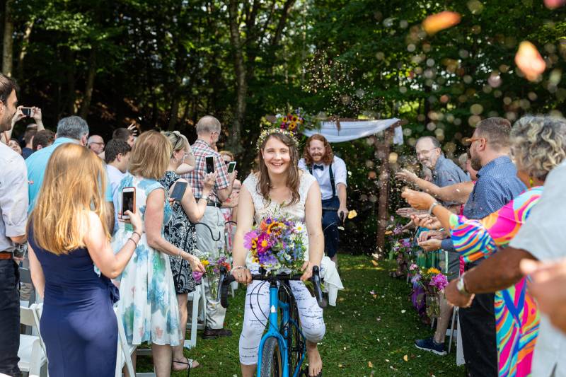 Couple riding bikes down the aisle during outdoor wedding