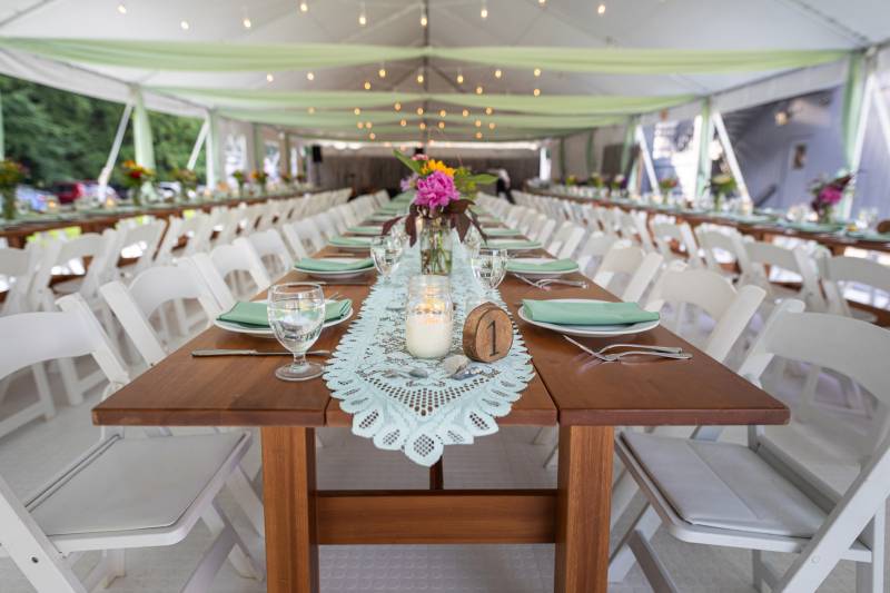 Table set up with table runner, wood table numbers and colorful flowers at outdoor tent summer weddi