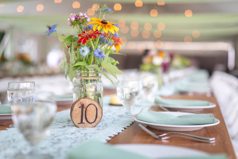 Table set up with table runner, wood table numbers and colorful flowers at outdoor tent summer weddi
