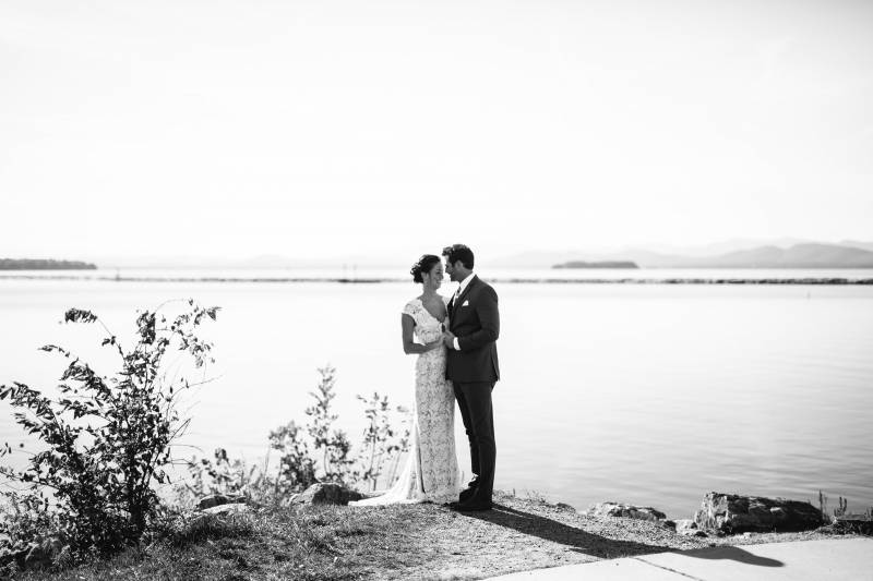 Black and white portrait of couple embracing by Lake Champlain on their wedding day