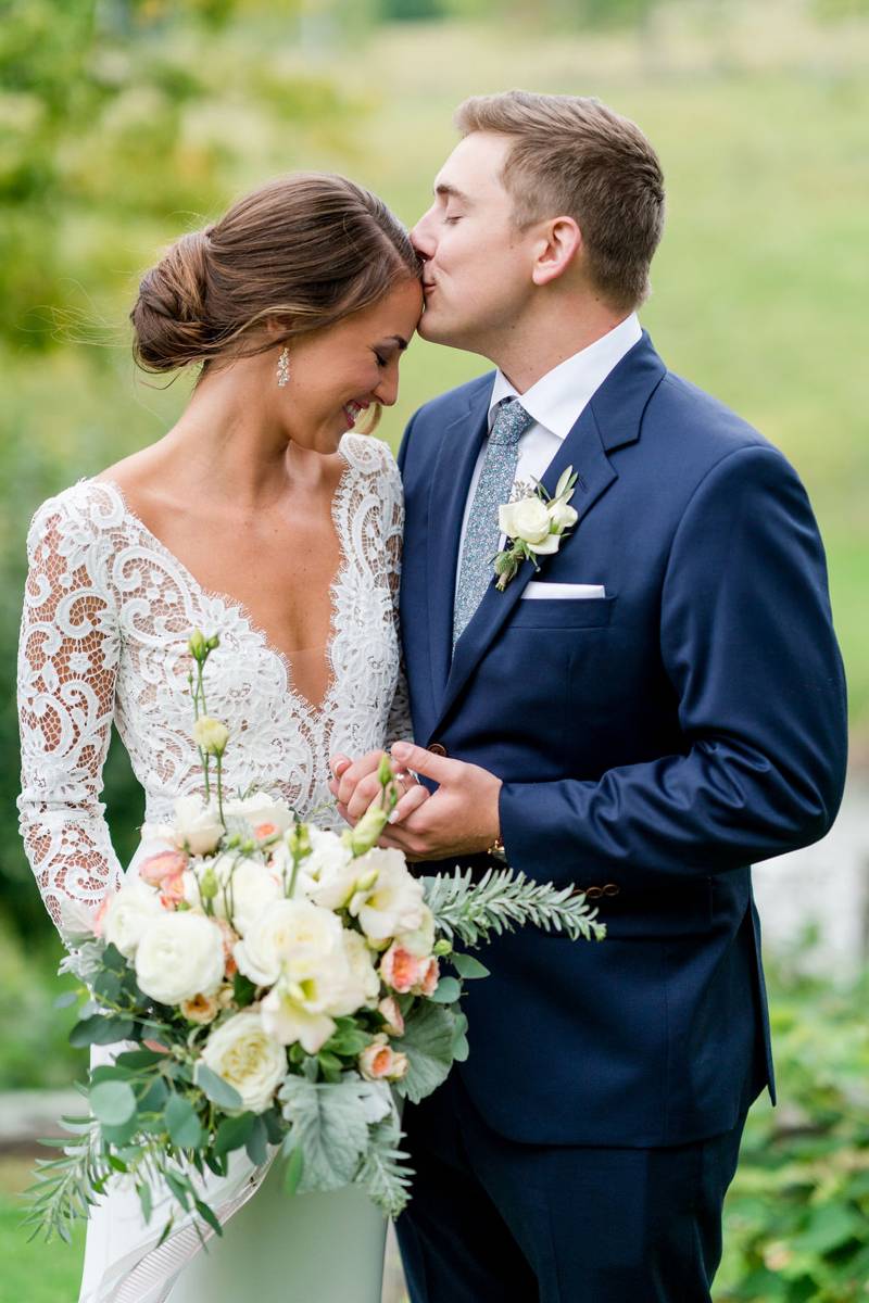 Couple kissing on their wedding day with a closeup on pastel bridal bouquet