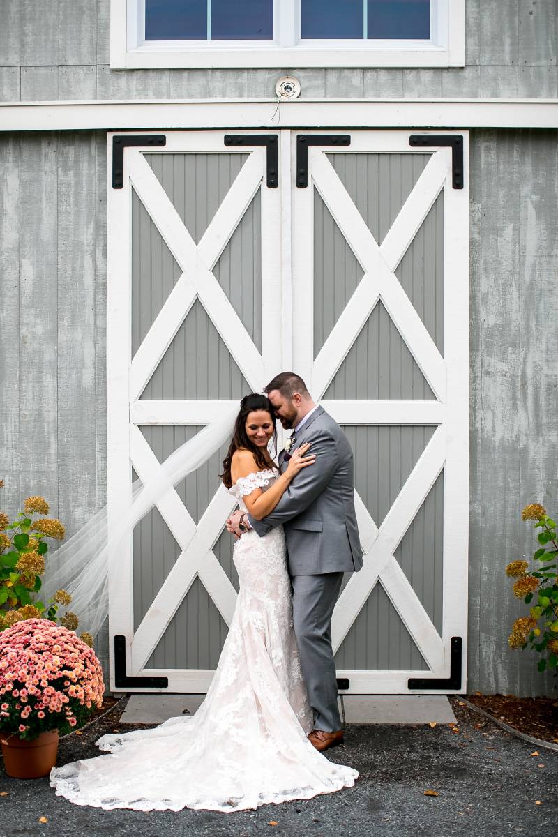 Barn backdrop wedding portrait of couple featuring the bride's long lace dress and long veil during 