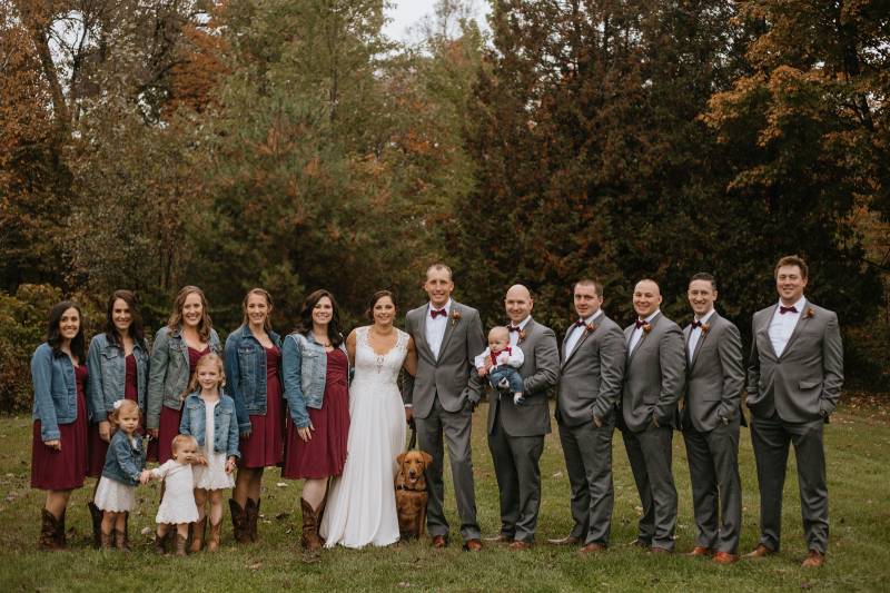 Wedding party portrait featuring burgundy bridesmaid dresses and cowboy boots and grey groomsmen sui