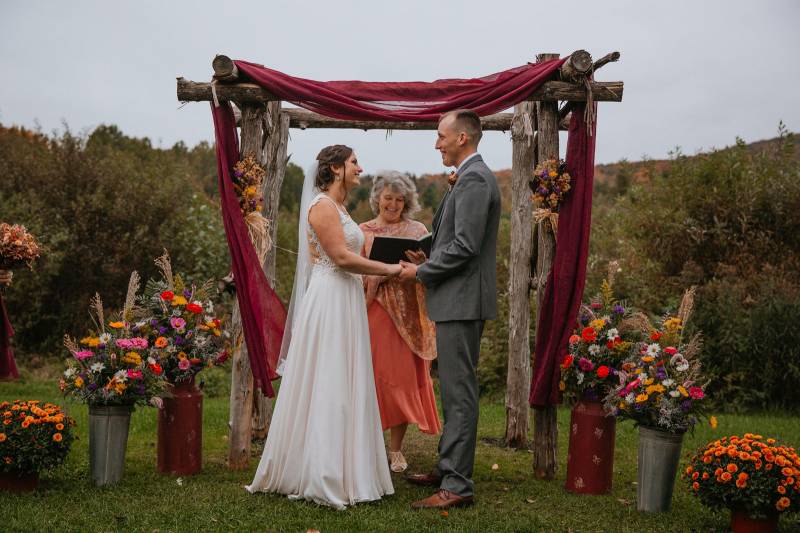 Outdoor wedding ceremony at the Mansfield Barn with burgundy draped arch and fall florals