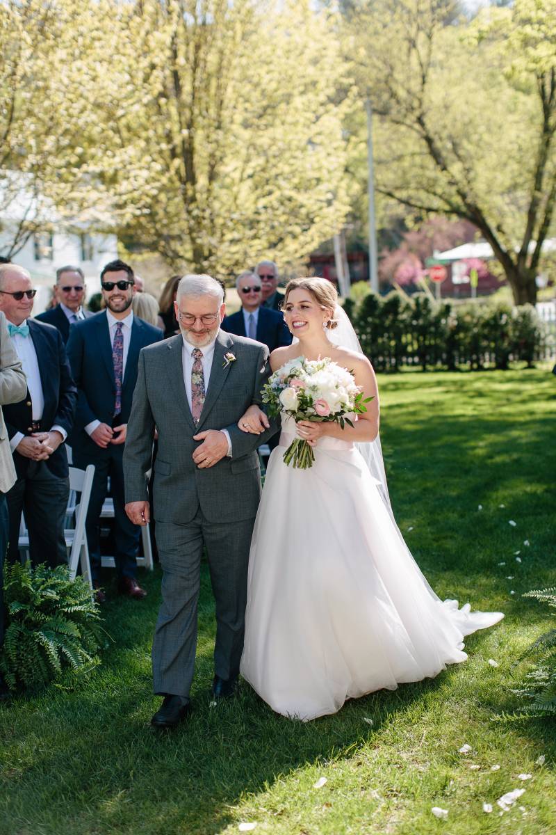 Bride walking down the aisle with father carrying lush green and pink bouquet